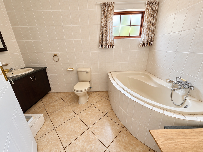 A functional bathroom featuring a corner bathtub, built-in vanity with basin, toilet, and neutral wall and floor tiling.