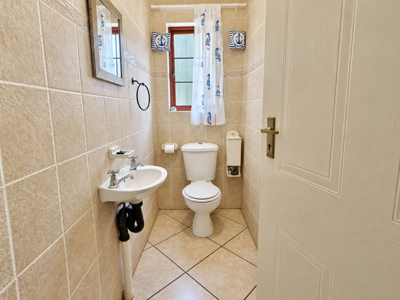 A compact guest bathroom featuring neutral ceramic wall and floor tiles, a pedestal basin, and a standard toilet.