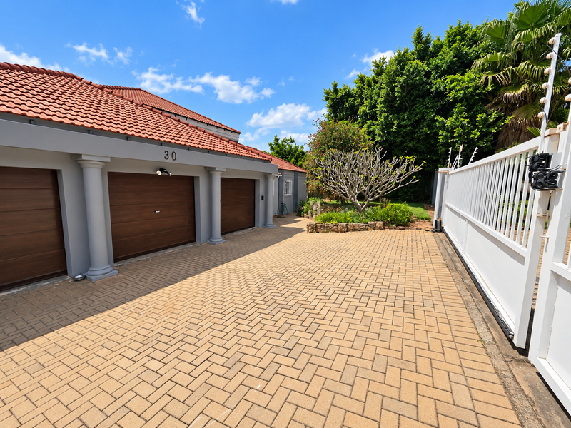 A well-maintained front exterior featuring a triple garage with wooden doors, paved driveway, and secure perimeter fencing with an automated gate.