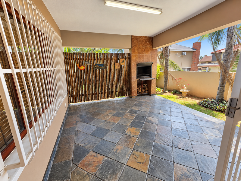 Covered patio area featuring tiled flooring, a built-in braai, and a bamboo privacy screen, offering a functional outdoor entertainment space.