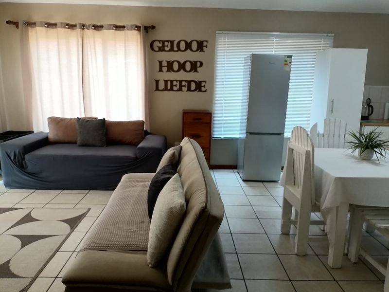 Open-plan living and dining area featuring neutral tiled flooring, large windows with venetian blinds, and a functional layout suitable for modern living.