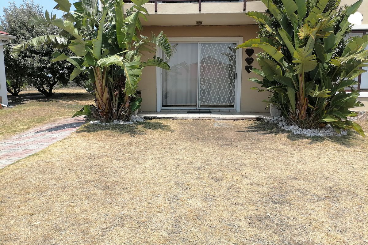 Rear view of the apartment featuring a sliding glass door with security gate, paved walkway, and access to an upper-level balcony.