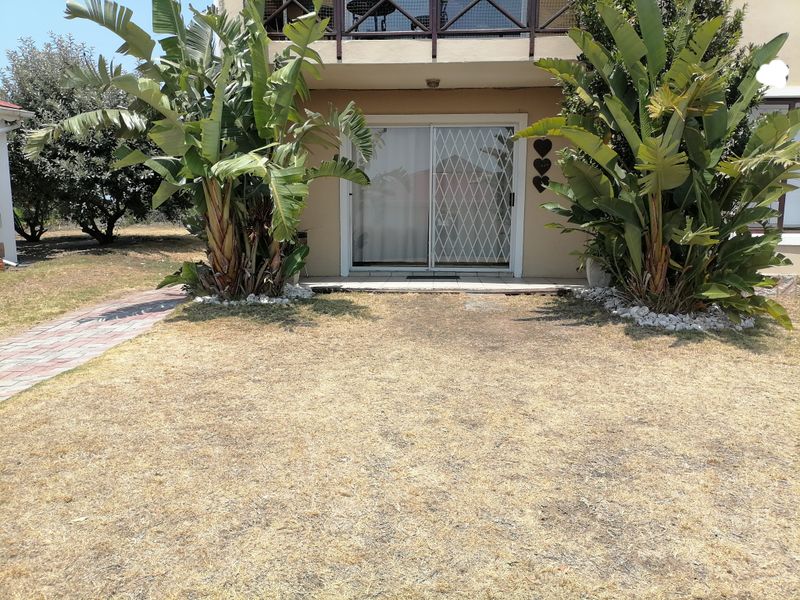 Rear view of the apartment featuring a sliding glass door with security gate, paved walkway, and access to an upper-level balcony.