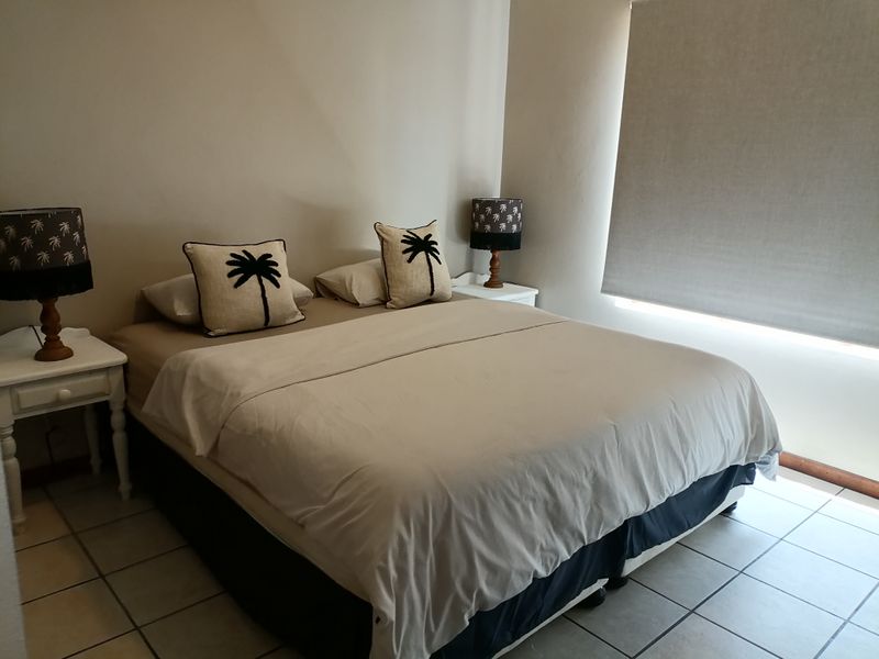A bedroom featuring neutral wall tones, tiled flooring, and a fitted roller blind for privacy.