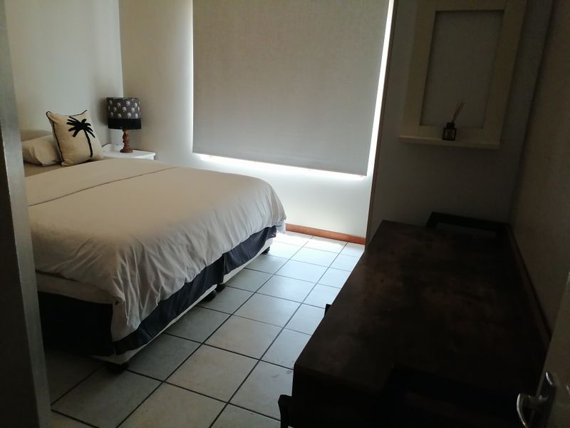 A functional bedroom featuring tiled flooring, a built-in wall niche, and a roller blind for privacy.