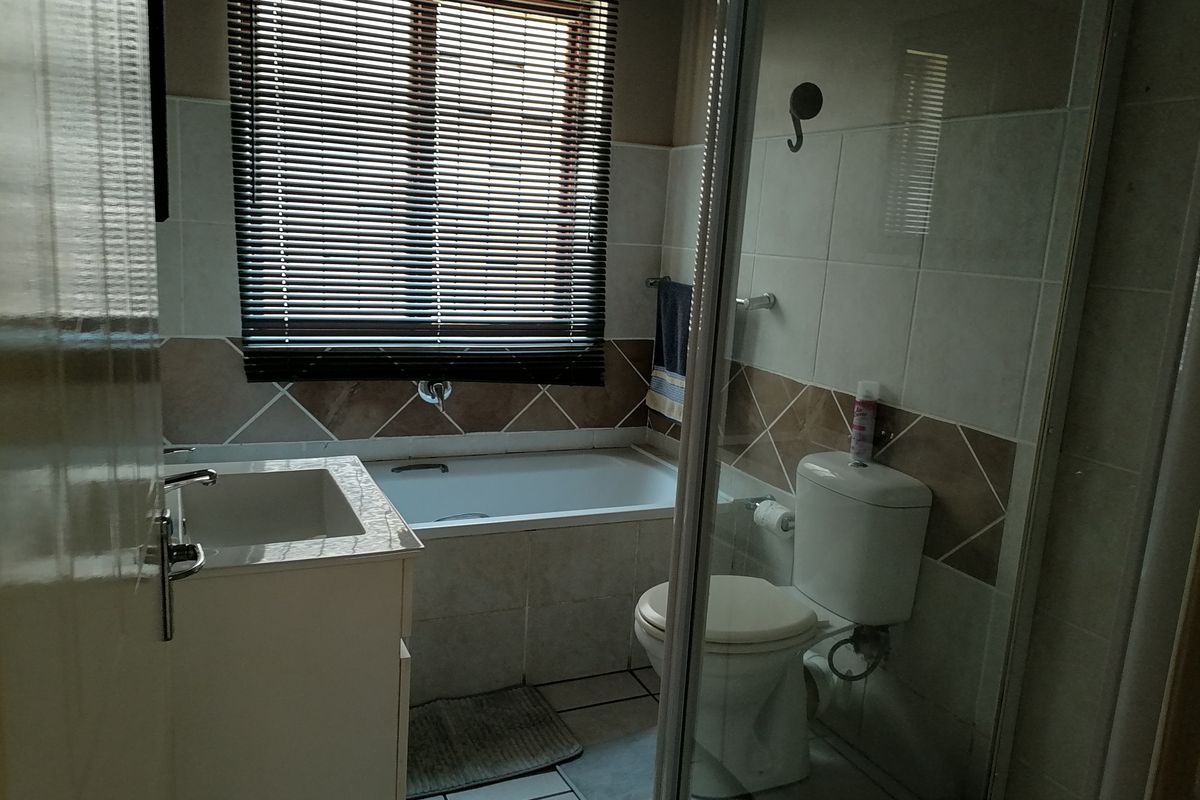 A functional bathroom featuring a built-in bathtub, vanity cabinet, toilet, and a glass-enclosed shower area with tiled finishes.