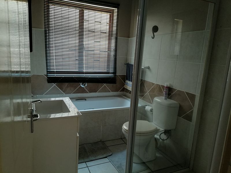 A functional bathroom featuring a built-in bathtub, vanity cabinet, toilet, and a glass-enclosed shower area with tiled finishes.