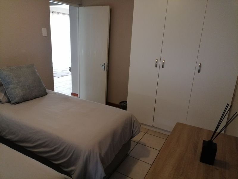 A bedroom featuring tiled flooring and a white built-in wardrobe, with an adjacent doorway leading to another room.