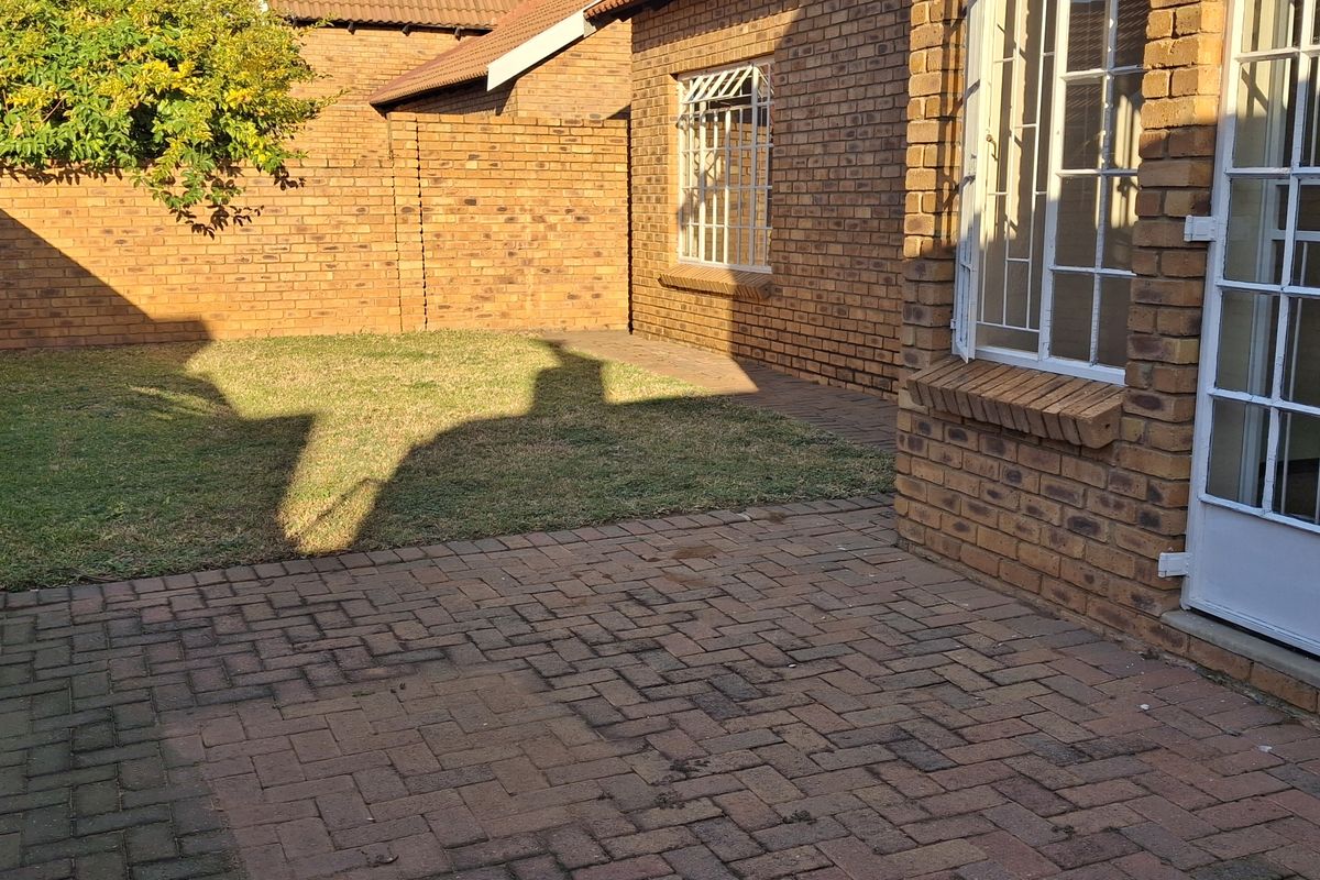 A private rear courtyard featuring facebrick walls, paved patio area, and a small lawn with security-fitted windows and doors.