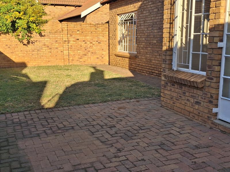 A private rear courtyard featuring facebrick walls, paved patio area, and a small lawn with security-fitted windows and doors.