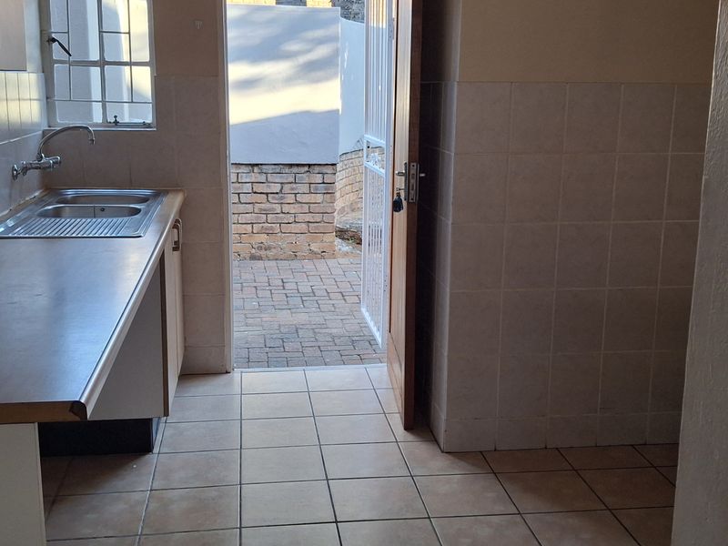 A functional scullery or utility area featuring a stainless steel sink, tiled splashbacks, and direct access to an outdoor paved courtyard.
