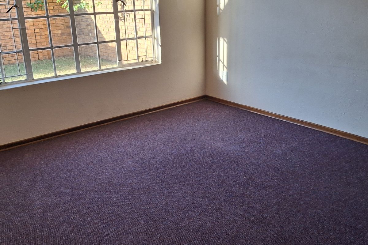 An empty bedroom featuring carpeted flooring and a large window with security burglar bars.