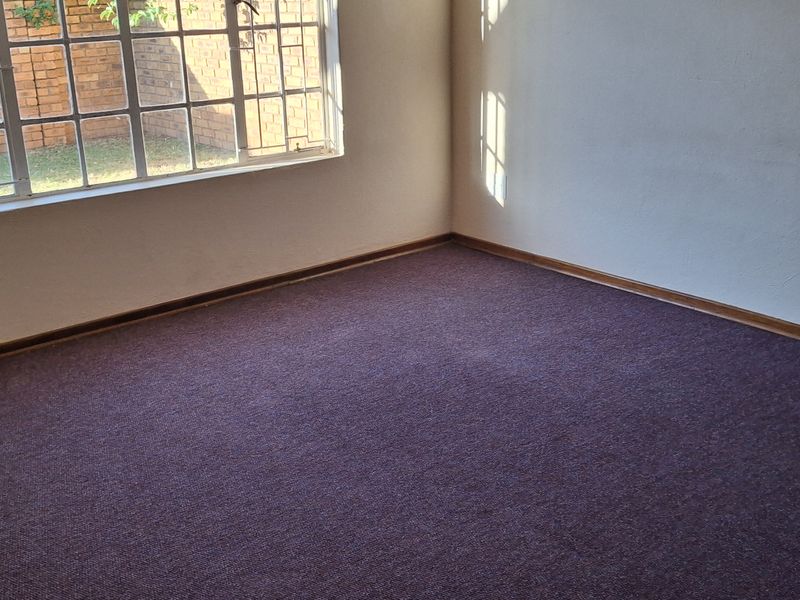 An empty bedroom featuring carpeted flooring and a large window with security burglar bars.