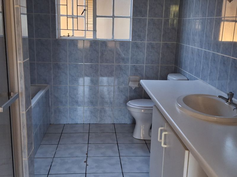 A dated bathroom featuring a built-in vanity, ceramic basin, toilet, and bathtub with full-height wall tiling and security bars on the window.