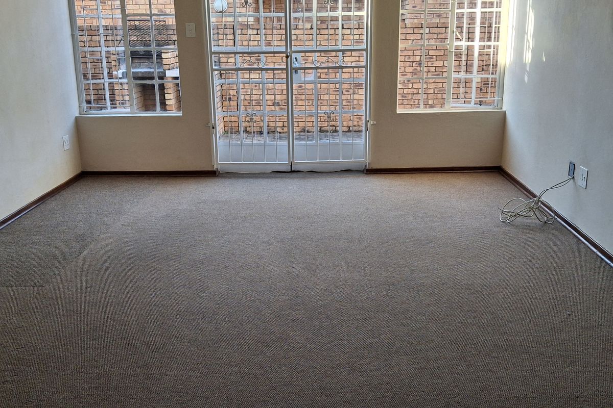 An empty living room featuring carpet flooring, security gates on the windows and doors, and neutral wall finishes.