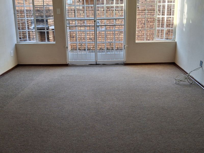 An empty living room featuring carpet flooring, security gates on the windows and doors, and neutral wall finishes.