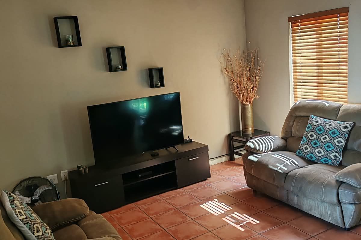 A comfortable living room featuring tiled flooring, an air conditioning unit, and natural light filtered through venetian blinds.