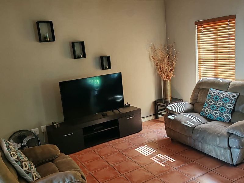 A comfortable living room featuring tiled flooring, an air conditioning unit, and natural light filtered through venetian blinds.
