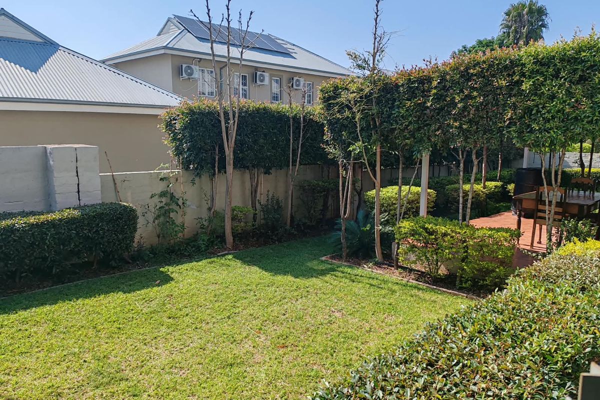 A private rear garden featuring a well-maintained lawn, mature hedges, and a boundary wall with a visible structural crack.