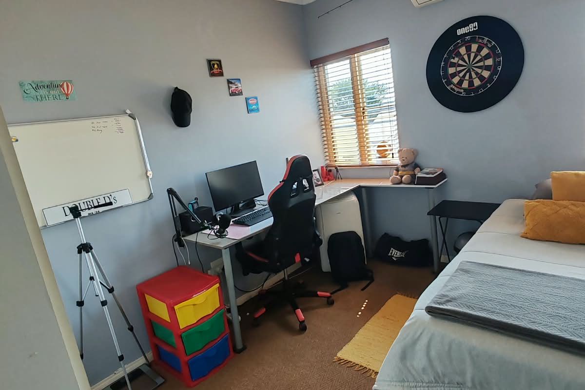 A functional bedroom featuring carpeted flooring, a wall-mounted split-system air conditioner, and window blinds, providing a comfortable space for rest or study.