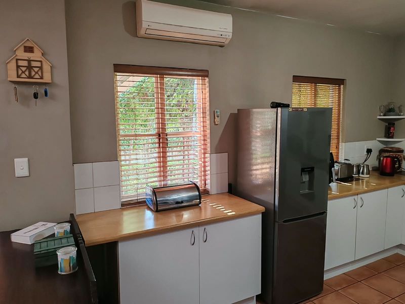 A functional kitchen featuring timber laminate countertops, white cabinetry, tiled splashbacks, and a wall-mounted split-system air conditioner.
