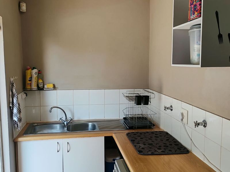 A functional scullery area featuring a stainless steel sink, laminate countertops, tiled splashbacks, and built-in cabinetry with wall-mounted storage.
