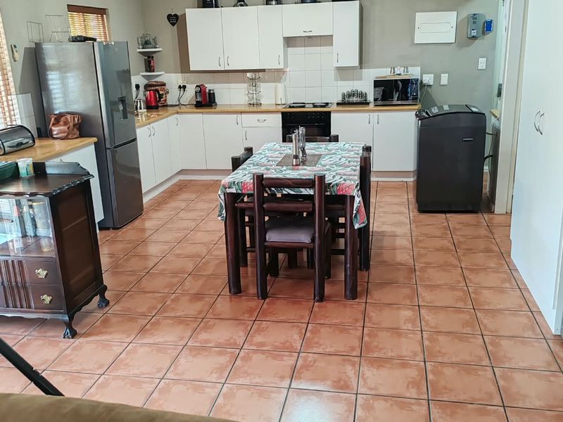 Open-plan kitchen and dining area featuring tiled flooring, white cabinetry, and integrated appliances, providing a functional space for cooking and casual dining.