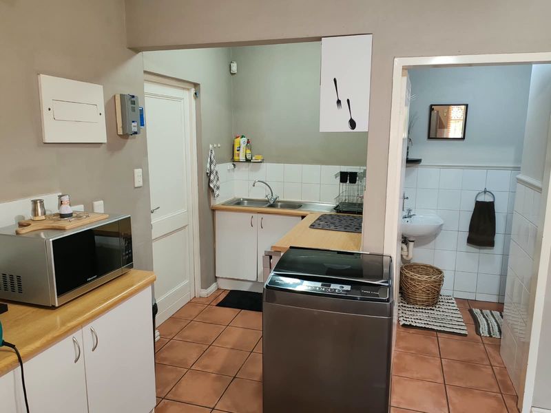 Functional laundry area featuring built-in cabinetry, a stainless steel sink, tiled splashback, and durable ceramic floor tiles, with an adjacent bathroom access.