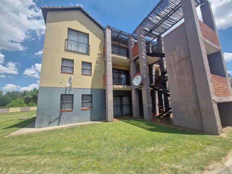 Exterior view of a multi-story apartment building featuring balconies, external staircases, and a shared garden area.