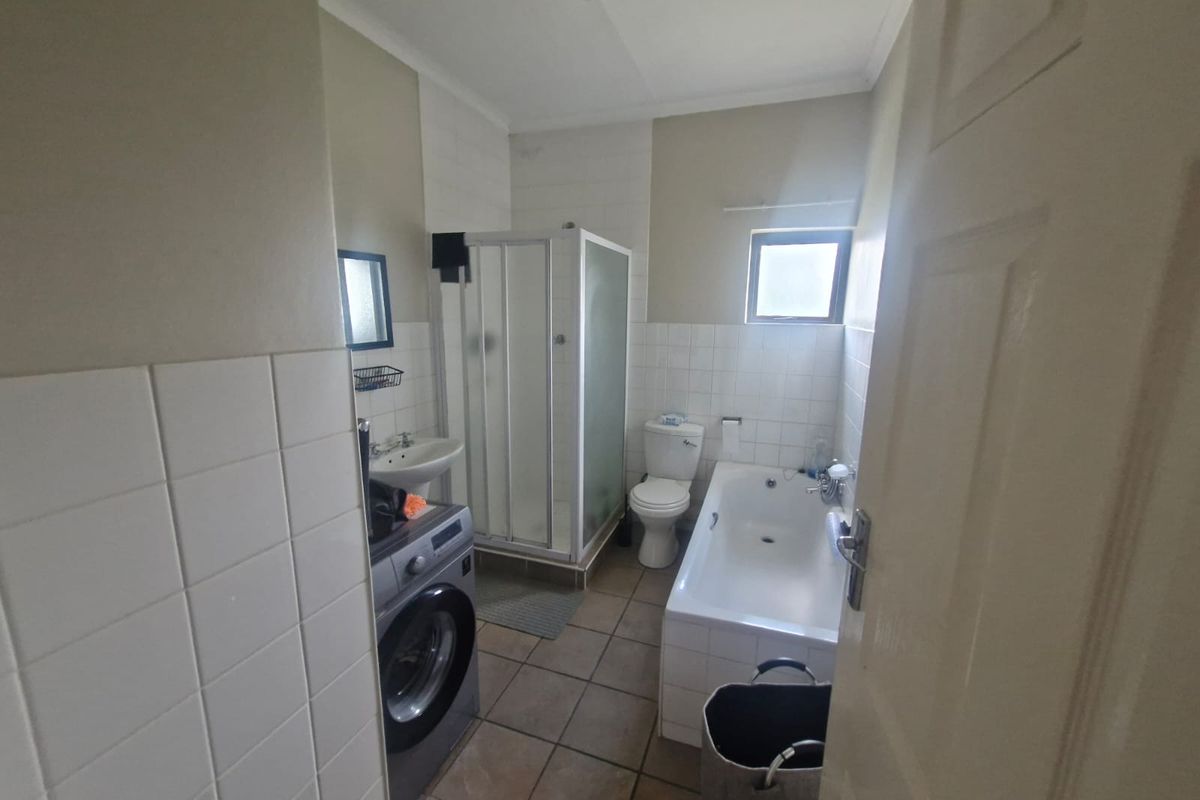 A functional bathroom featuring a shower enclosure, bathtub, pedestal basin, and toilet with neutral wall and floor tiling.