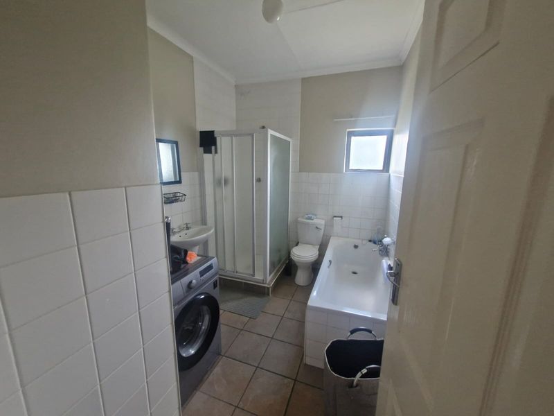 A functional bathroom featuring a shower enclosure, bathtub, pedestal basin, and toilet with neutral wall and floor tiling.