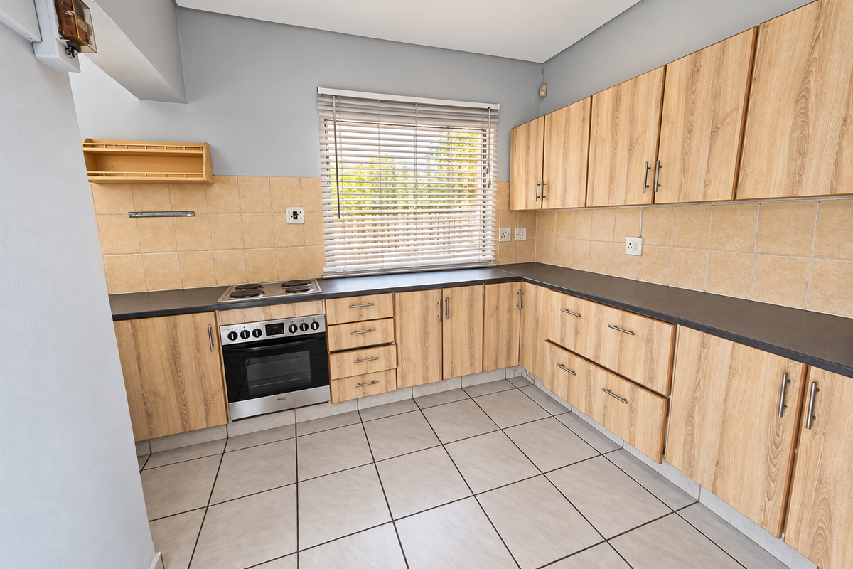 A clean, functional kitchen featuring light wood-finish cabinetry, dark countertops, a built-in oven and hob, and neutral tiled flooring.