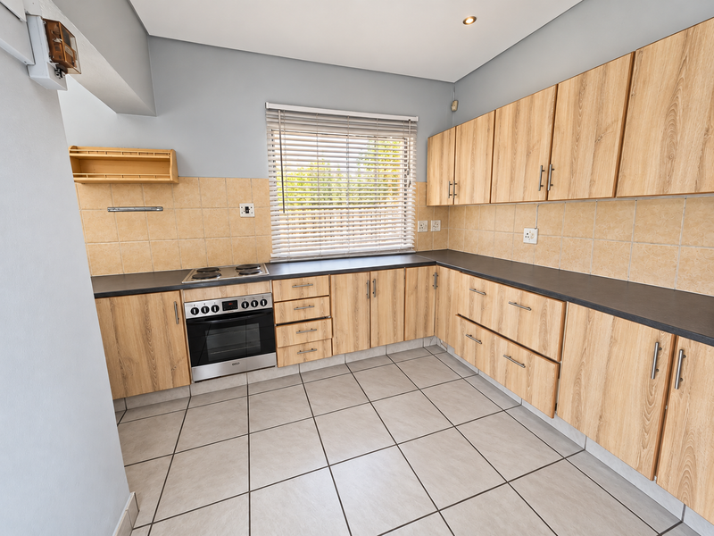 A clean, functional kitchen featuring light wood-finish cabinetry, dark countertops, a built-in oven and hob, and neutral tiled flooring.