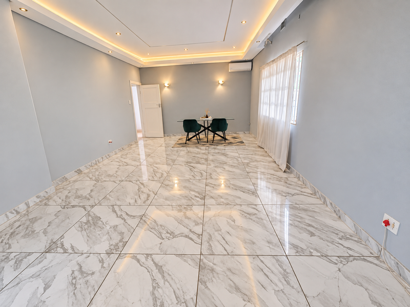 A bright and modern living area featuring polished marble-look floor tiles, recessed cove lighting, and a wall-mounted air conditioning unit.