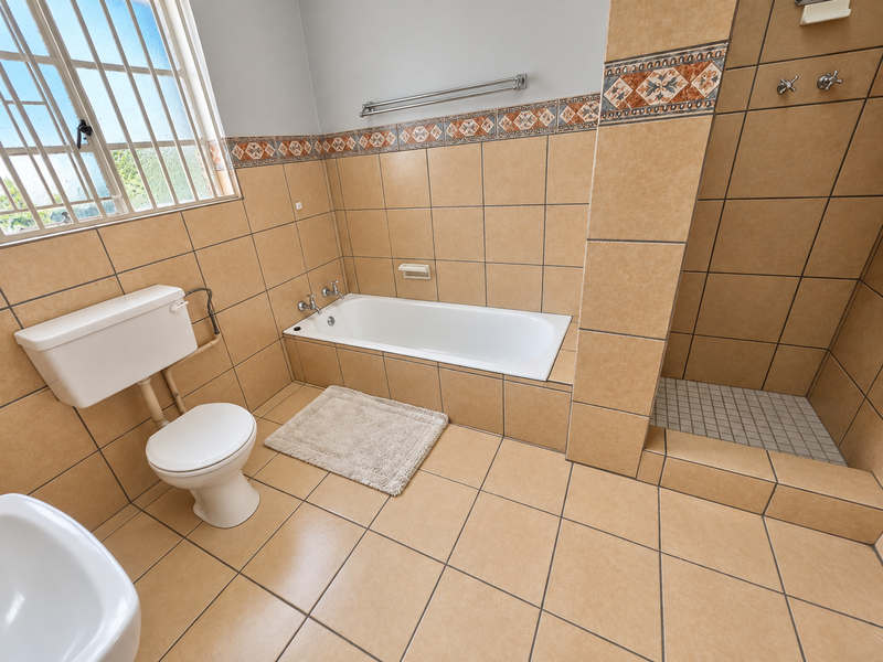 A functional bathroom featuring a built-in bathtub, separate walk-in shower, and neutral ceramic tiling throughout.
