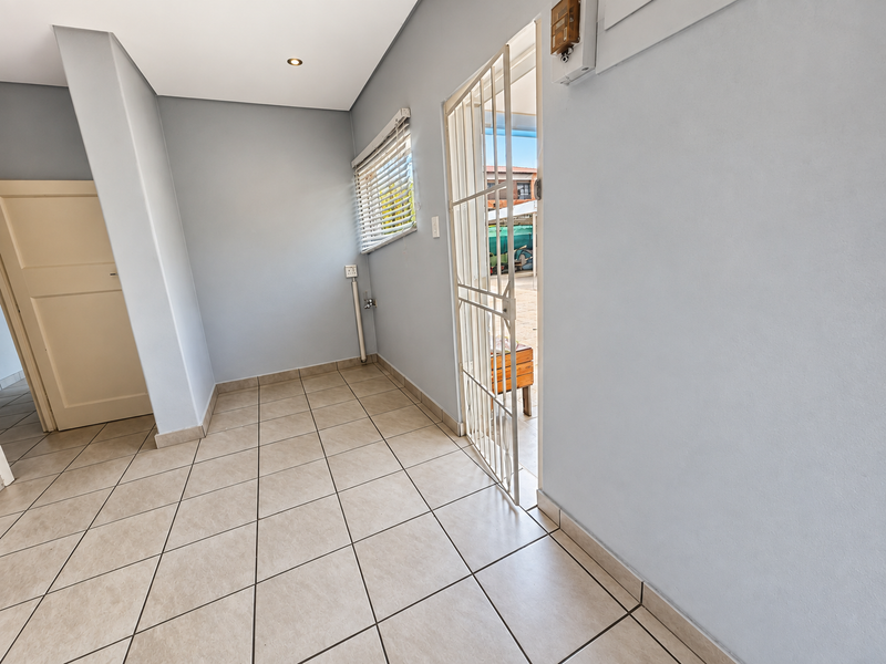 A clean, empty entrance area featuring neutral tiled flooring, recessed lighting, and a secure metal gate leading to the exterior.