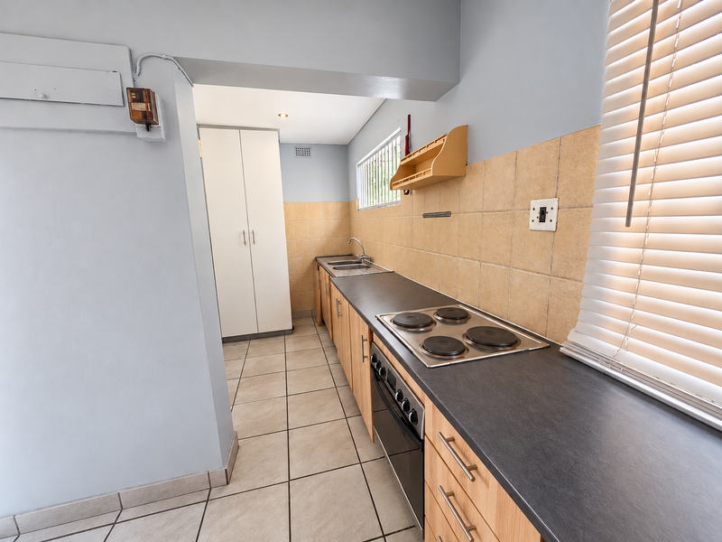 A functional kitchen featuring light wood cabinetry, dark countertops, a built-in oven and hob, and neutral tiled finishes throughout.