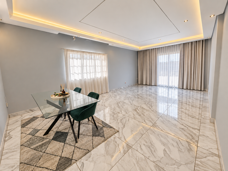 Spacious living area featuring high-end marble-look floor tiles, elegant recessed cove lighting, and floor-to-ceiling curtains leading to a bright outdoor space.