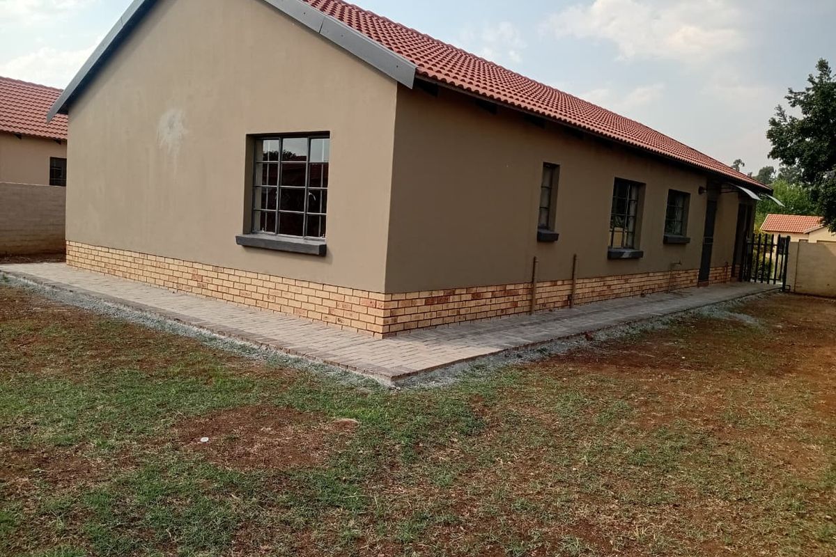 A view of the rear exterior of the house featuring a tiled roof, brick plinth detailing, and a paved walkway surrounding the structure.