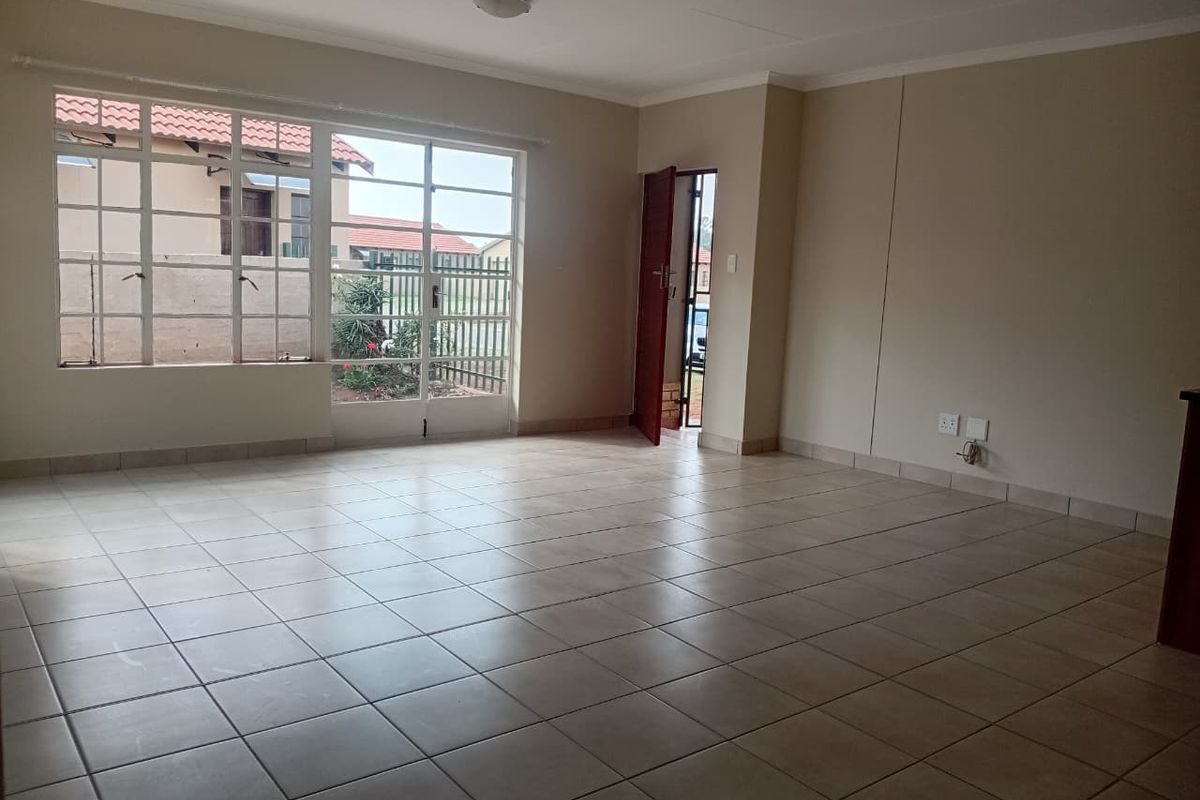 A spacious, empty living area featuring neutral tiled flooring, large windows for natural light, and direct access to the exterior.