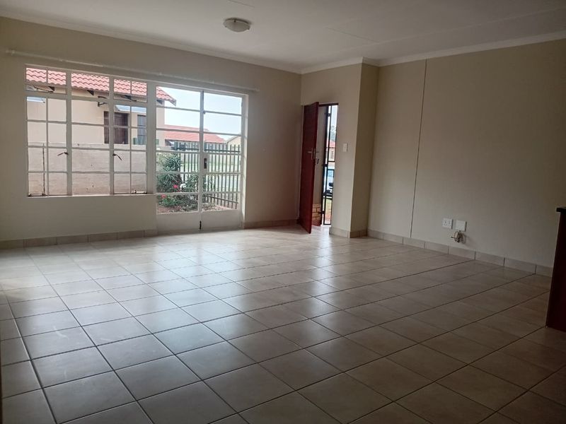 A spacious, empty living area featuring neutral tiled flooring, large windows for natural light, and direct access to the exterior.