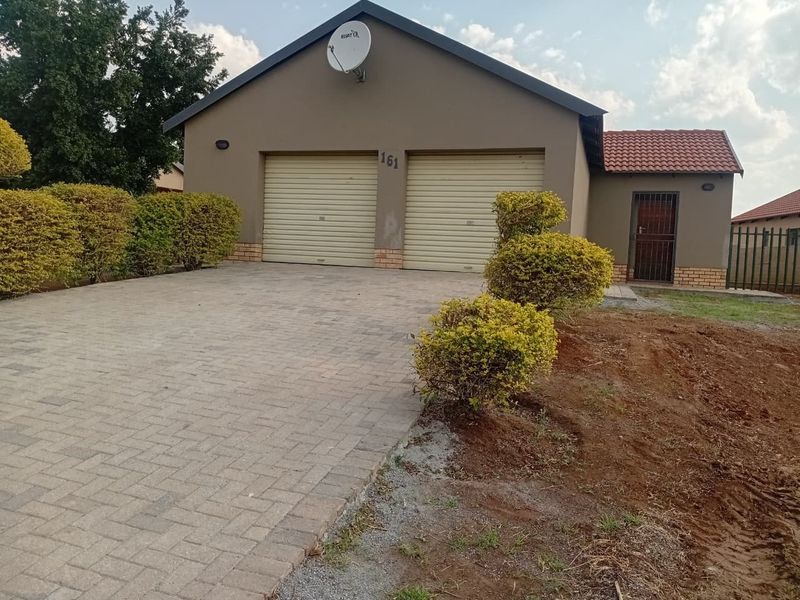 Front view of a residential property featuring a double garage, paved driveway, and secure entrance door.