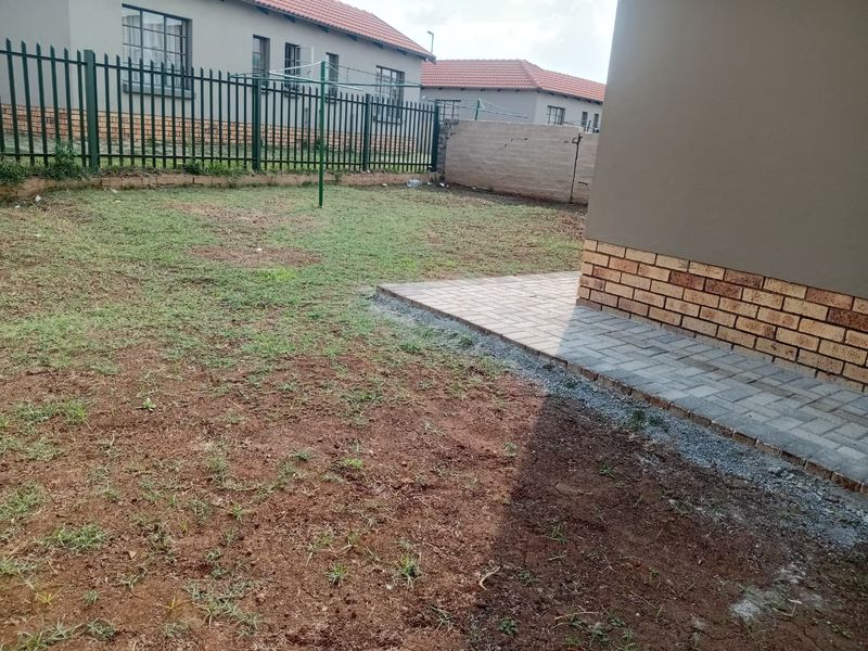Rear garden area featuring a paved patio, perimeter metal fencing, and an established lawn area requiring further landscaping.