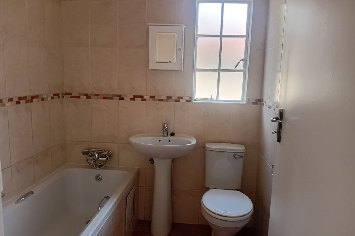A functional bathroom featuring a pedestal basin, bathtub, and toilet with neutral wall tiling and a window for natural light.