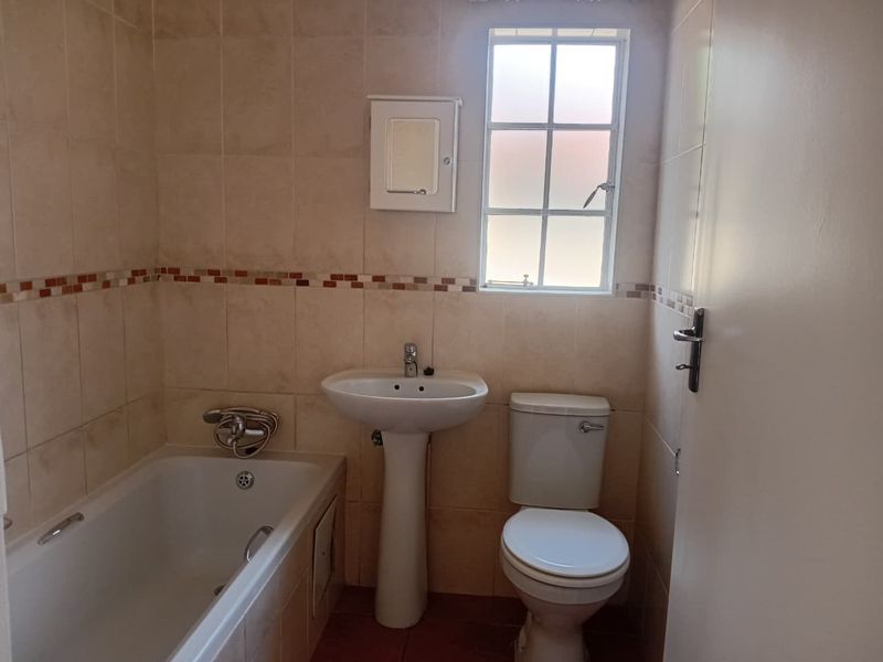 A functional bathroom featuring a pedestal basin, bathtub, and toilet with neutral wall tiling and a window for natural light.