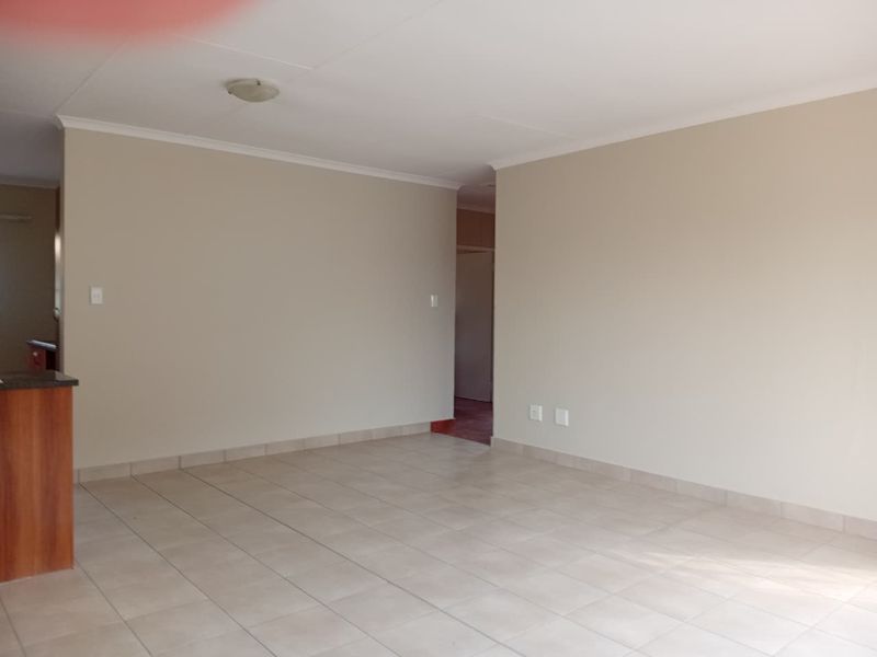 A spacious, neutral open-plan living area featuring tiled flooring, coved cornicing, and a breakfast bar, offering a clean and versatile blank canvas.