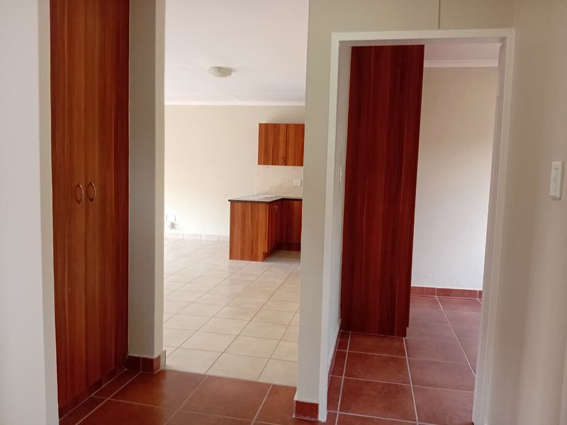 An open-plan living and kitchen area featuring tiled flooring, built-in wooden cabinetry, and ample storage space in a neutral, well-maintained interior.