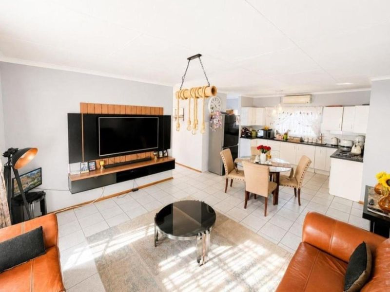 An open-plan living and dining area featuring tiled flooring, a built-in media console, and a functional kitchen with ample cabinetry.