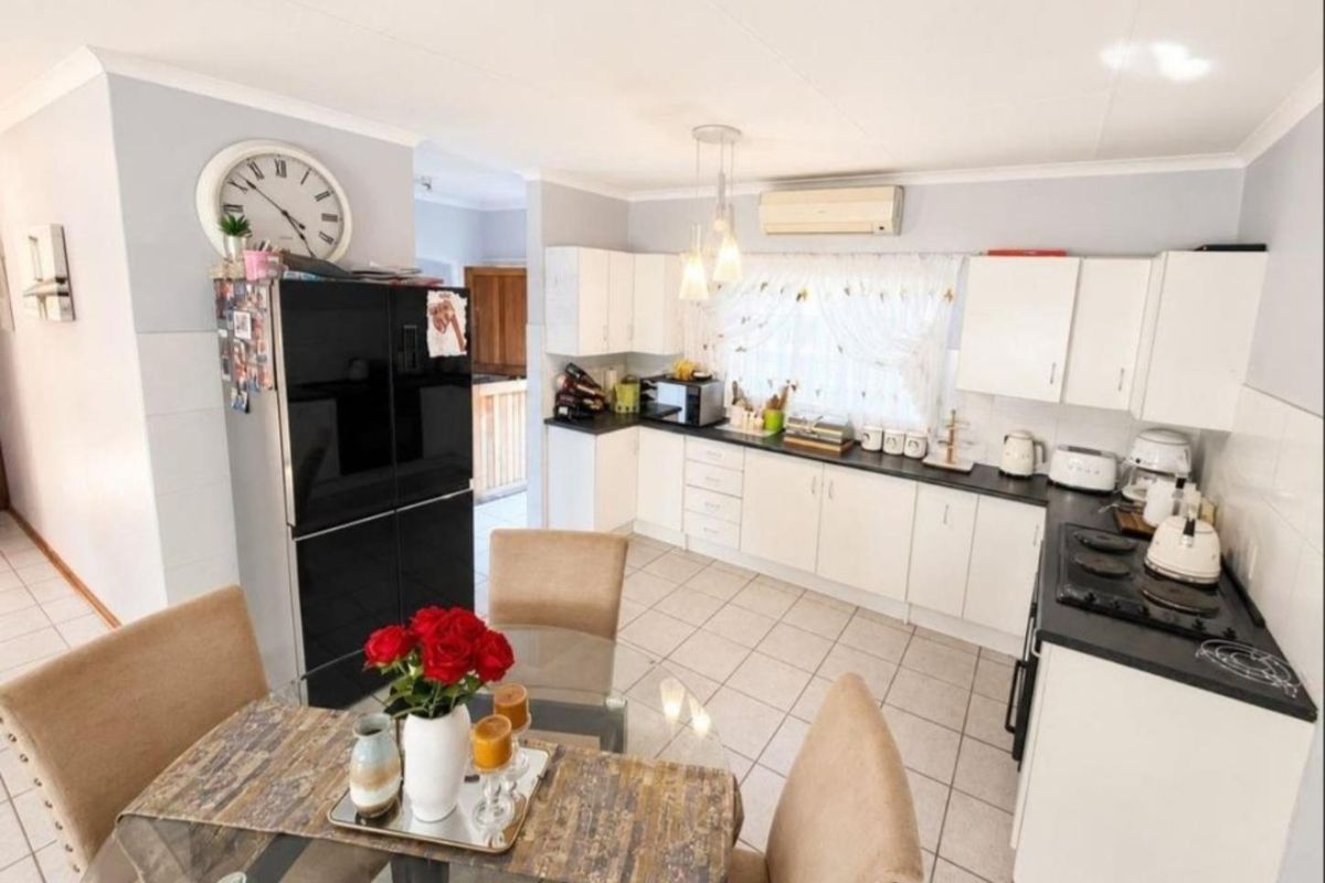A functional kitchen featuring white cabinetry, dark countertops, a gas hob, and tiled flooring, with an integrated air conditioning unit for climate control.