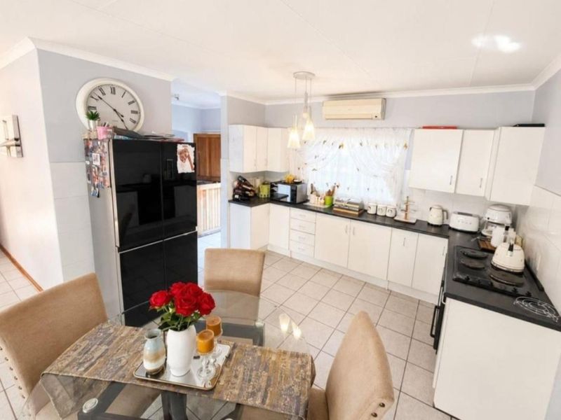 A functional kitchen featuring white cabinetry, dark countertops, a gas hob, and tiled flooring, with an integrated air conditioning unit for climate control.